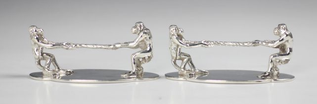 A near pair of silver plated novelty knife rests, the terminals designed as apes playing 'tug of
