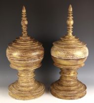 A pair of Burmese style turned wood urns and covers, each modelled with a distressed finish, gilt