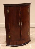A George III mahogany bowfront hanging corner cupboard, with a moulded cornice over a pair of