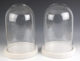 A pair of cylindrical glass domes on white ceramic stands, 20th century, each 40cm high including