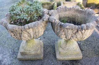 A pair of reconstituted leaf moulded urn planters, each raised upon an integral stepped plinth base,