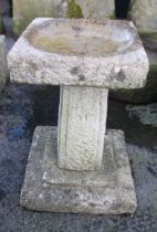 A reconstituted stone bird bath, the square top with a shallow circular well upon a pedestal of