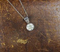 A diamond solitaire pendant, the round cut diamond set within a white metal rub over mount, with