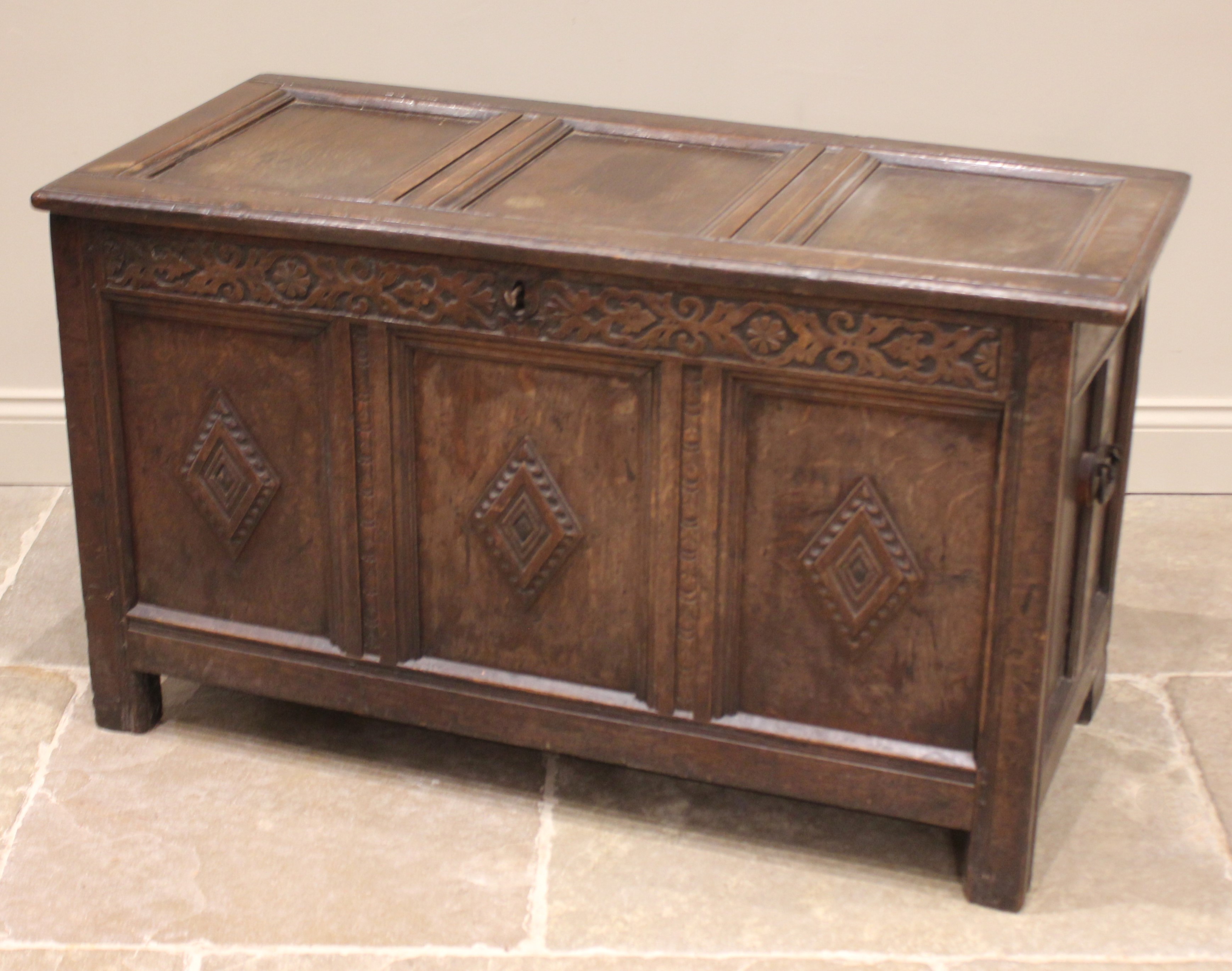 A late 17th/early 18th century oak coffer, the hinged cover over a carved frieze and three panels