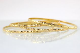 A set of three yellow metal bangles, all with star engraved continuous detail, stamped