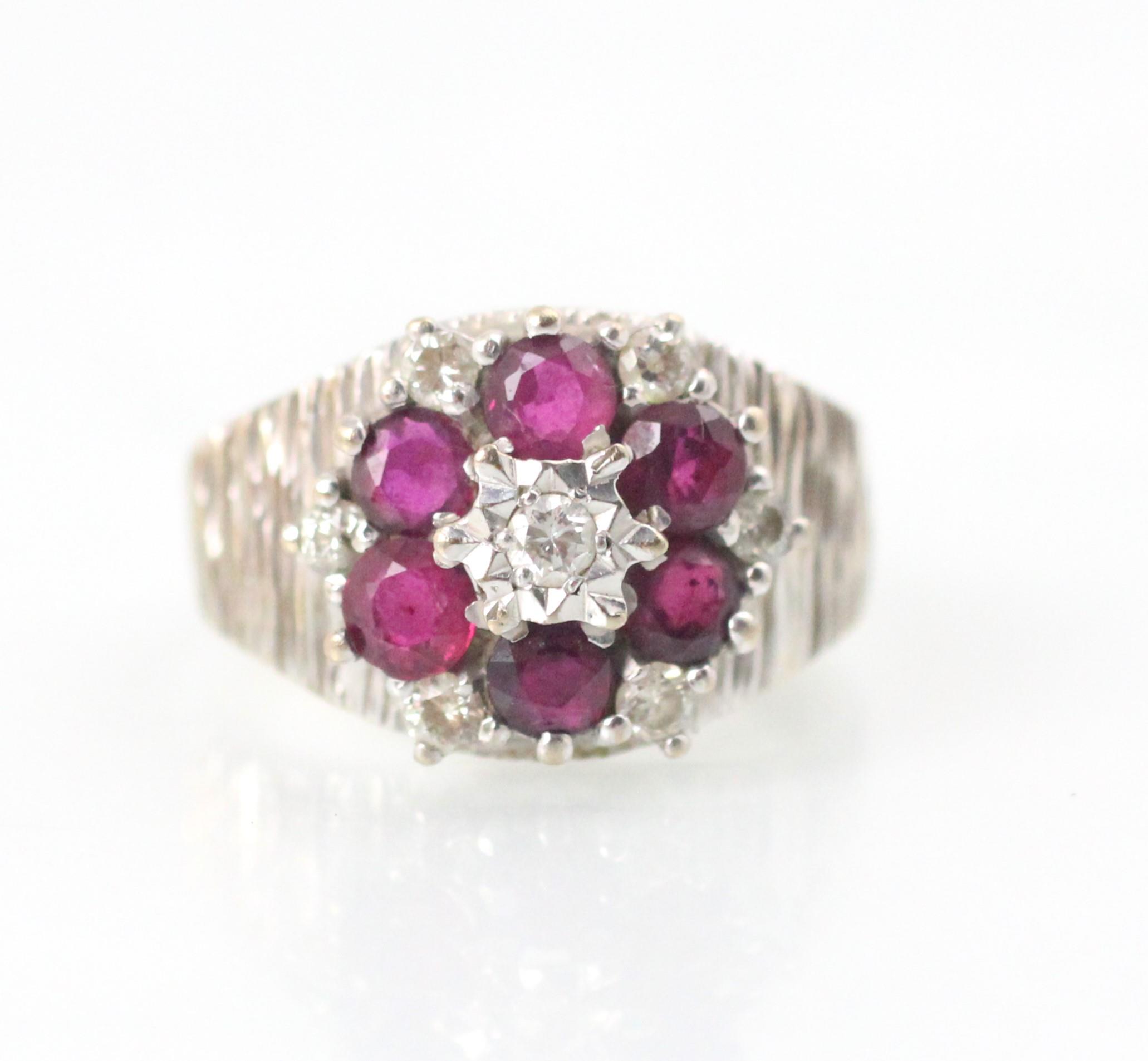 An 18ct white gold untested ruby and diamond cluster ring, the central round cut diamond with