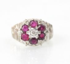 An 18ct white gold untested ruby and diamond cluster ring, the central round cut diamond with