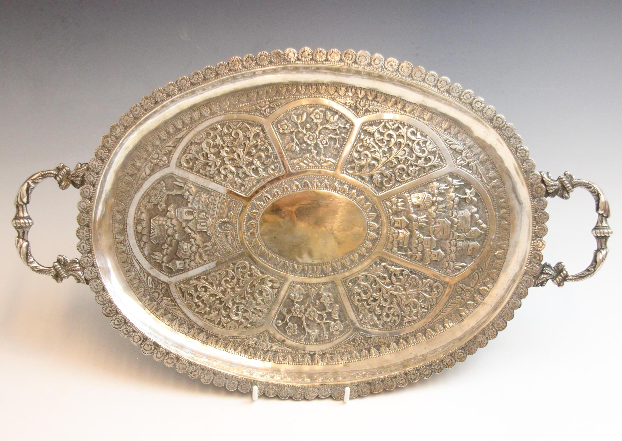 An Indian silver coloured tray, the cast twin handles above oval body decorated in embossed floral