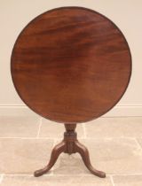 A George III mahogany tilt top tripod table, the circular top with a raised moulded rim upon a cup