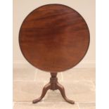 A George III mahogany tilt top tripod table, the circular top with a raised moulded rim upon a cup