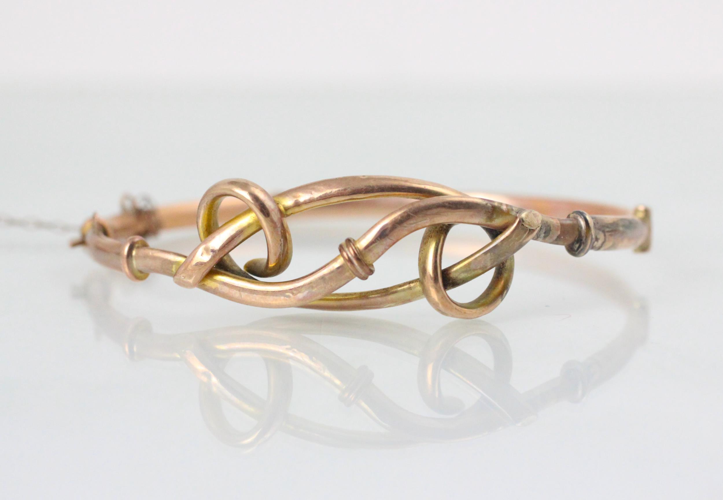 A yellow metal bangle, the hollow bangle with openwork bow style front, stamped ‘9ct’ suspending a