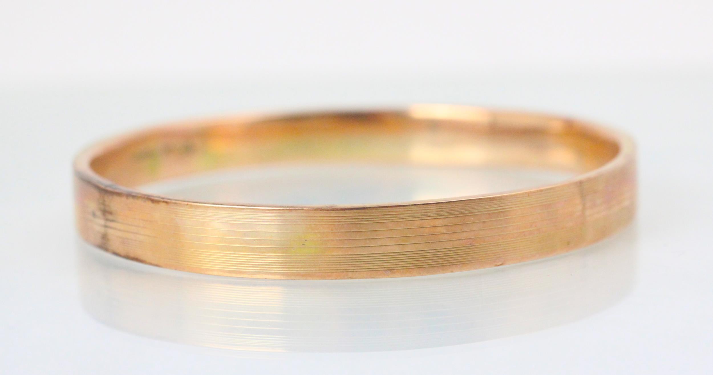 A 9ct yellow gold bangle, the hollow bangle with engine turned detail to exterior, 8cm wide, 14gms