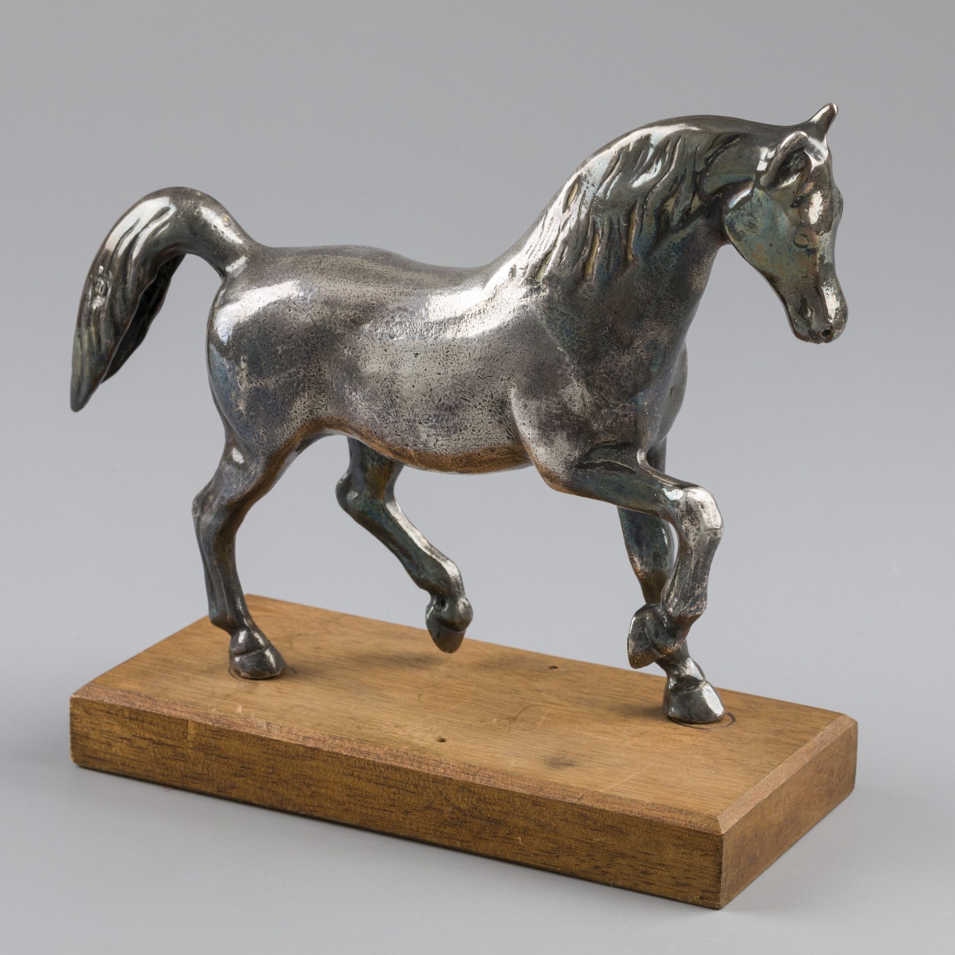 Miniature silver horse on wooden pedestal.