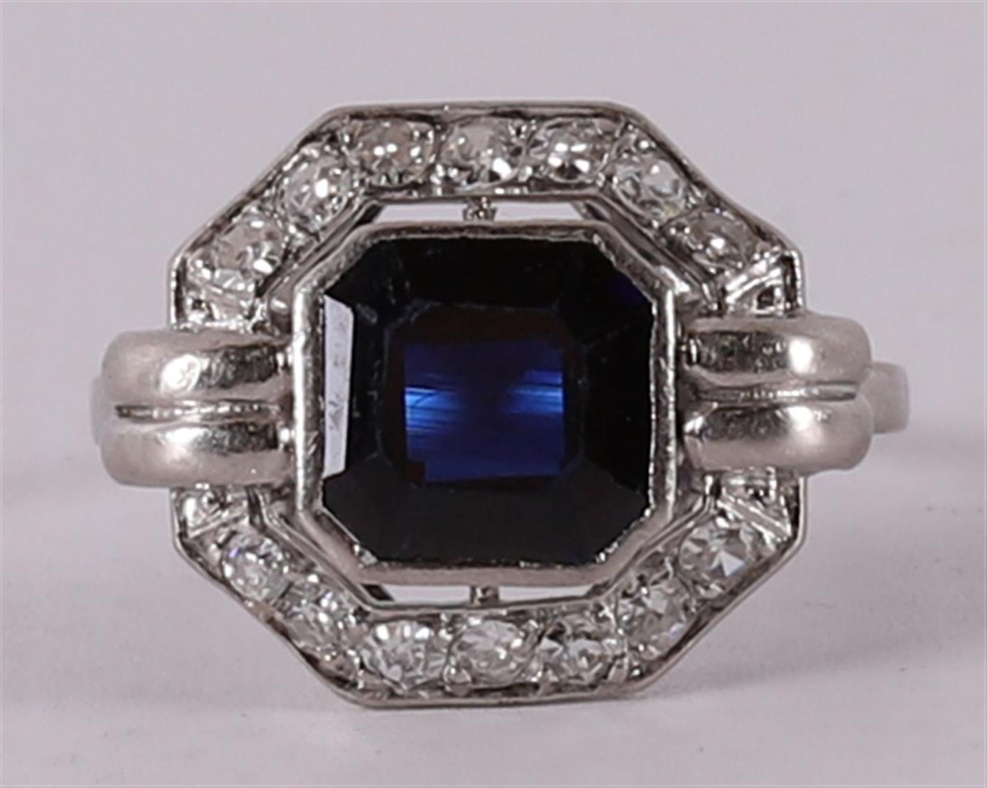 A platinum Art Deco ring with a facet cut blue sapphire and 14 diamonds.