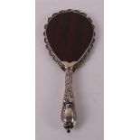 A hand mirror in silver frame with embossed floral decor.