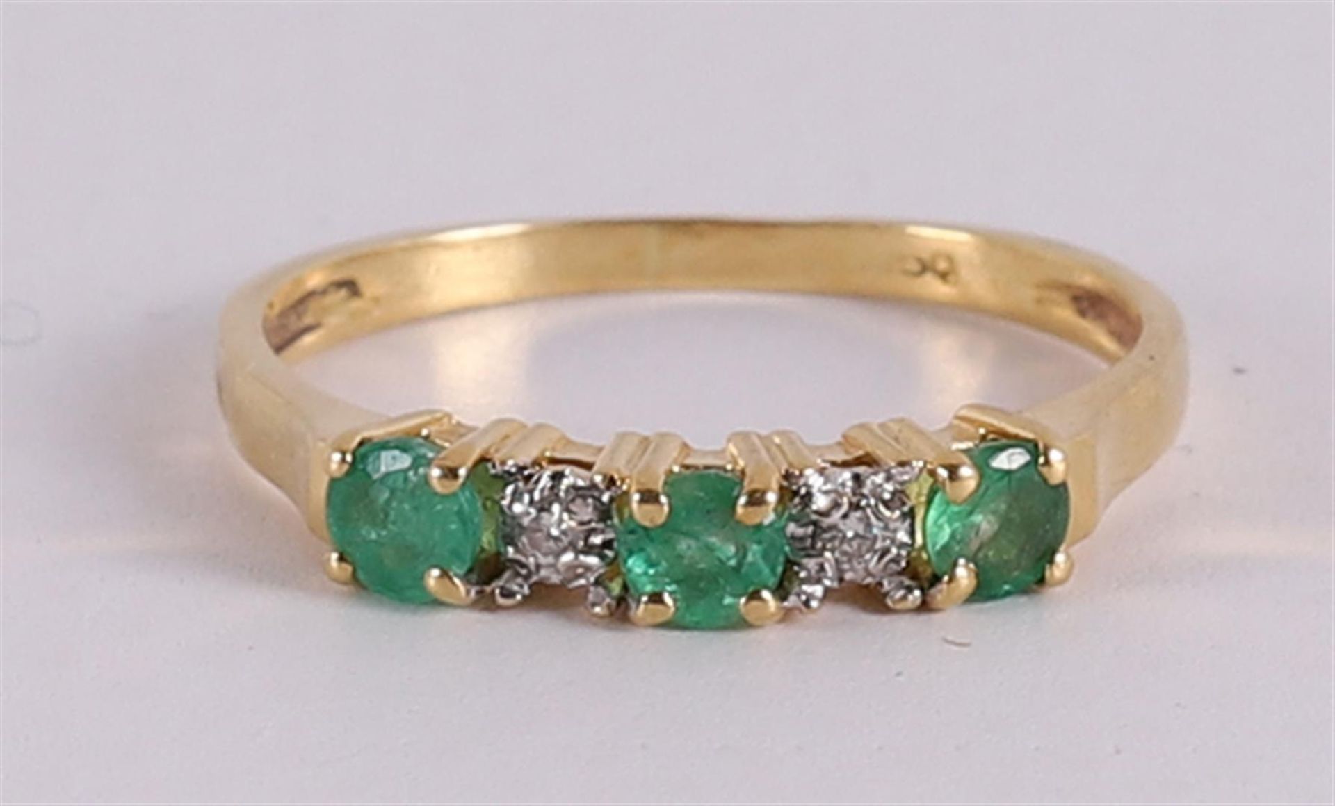 An 18 kt gold row ring with 3 facet cut emeralds and 2 brilliants