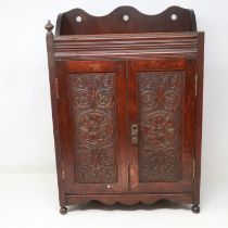 Carved oak smokers cabinet with pipe racks and two drawers, lacking one finial, H: 45 cm. Not