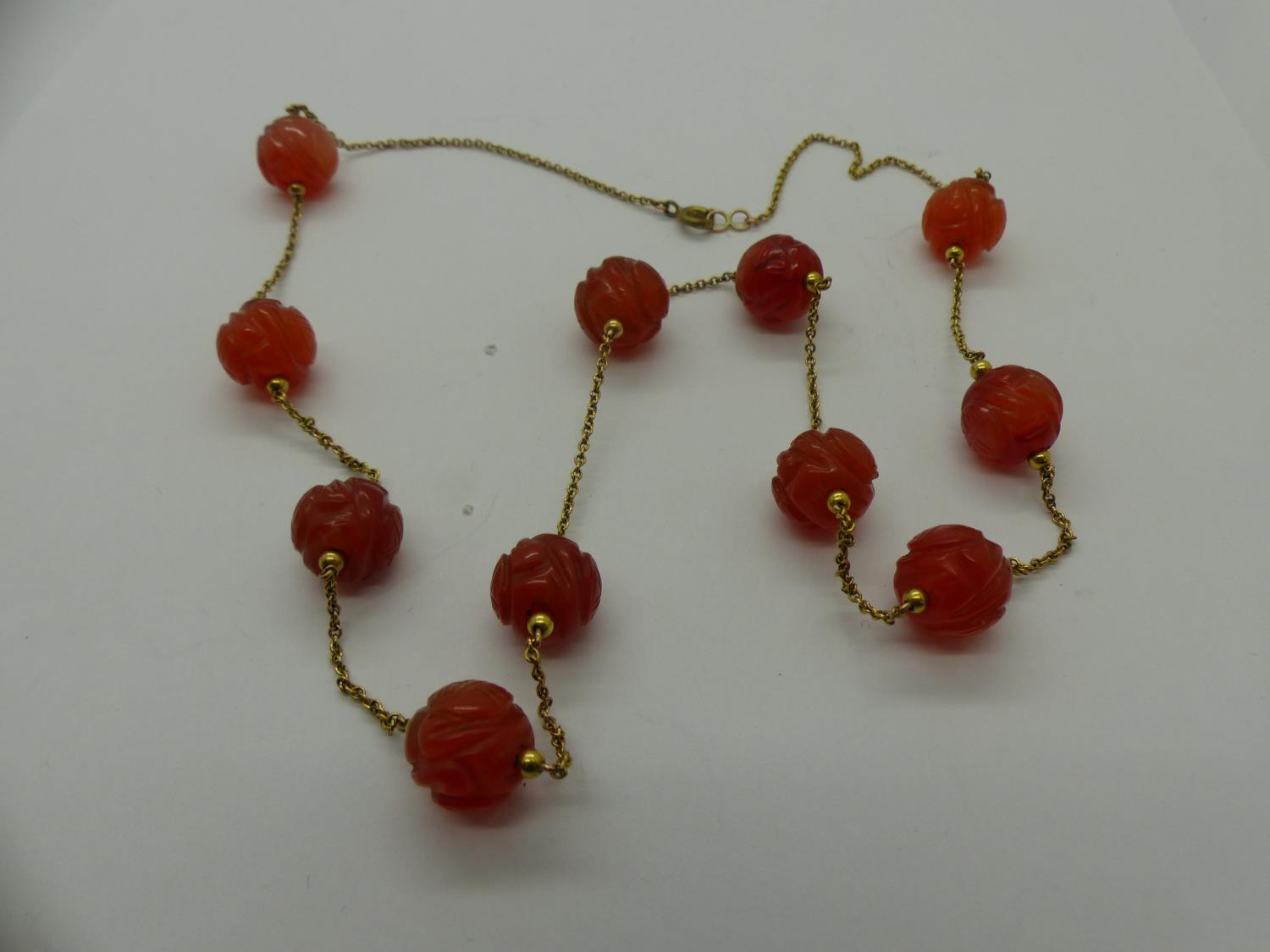 Unusual 19th century unmarked gold necklace, set with eleven carved carnelian beads, L: 63 cm. UK