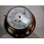 Modern brass barometer in the from of ships clock mounted on a polished mahogany base, by Sewills of