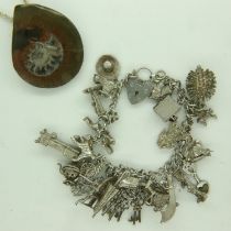 Silver charm bracelet mounted with twenty-five charms, 66g, and a fossil pendant on a silver neck