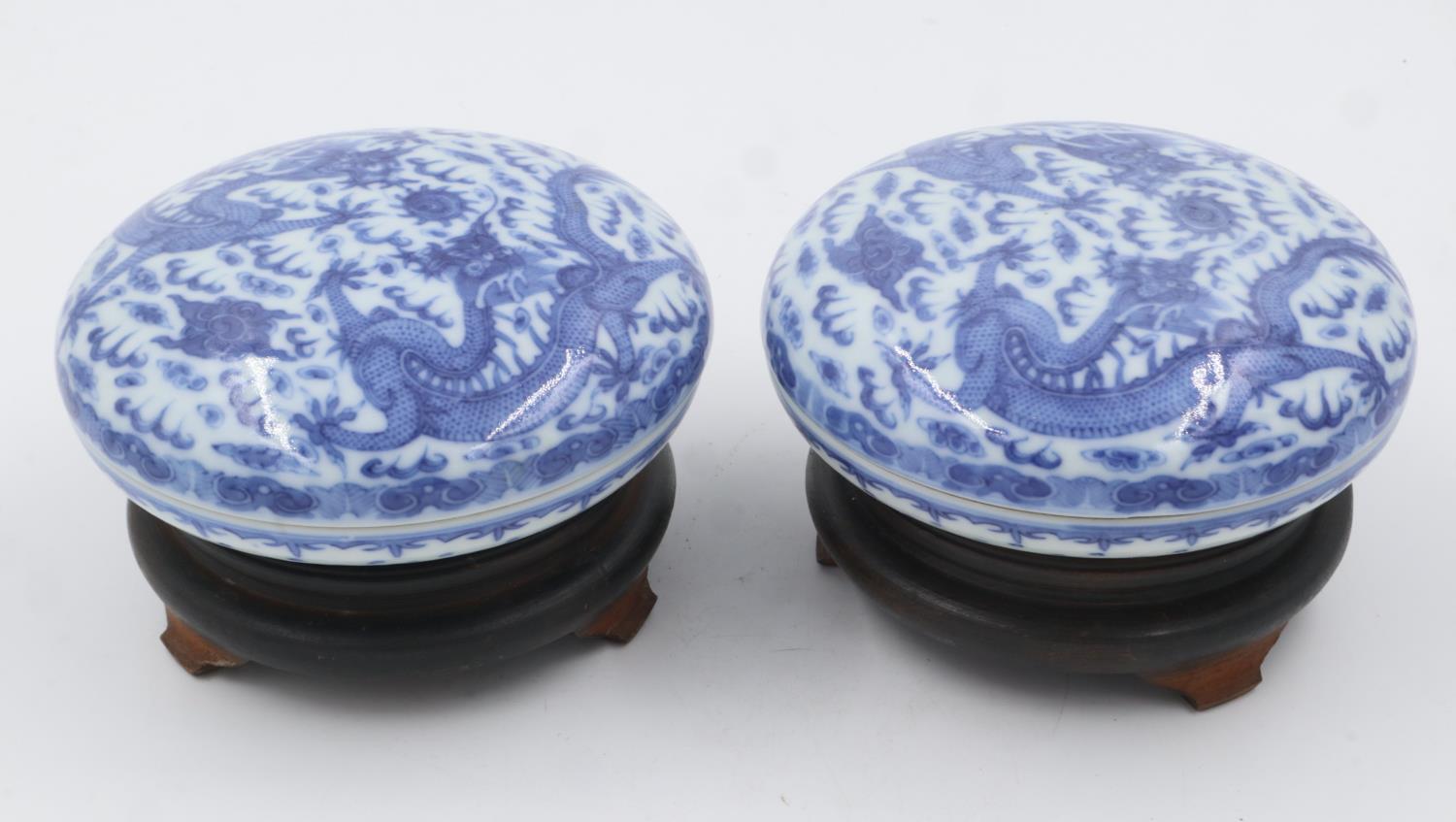 Pair of Chinese blue and white covered bowls with dragon decoration, each raised on a wooden