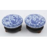 Pair of Chinese blue and white covered bowls with dragon decoration, each raised on a wooden