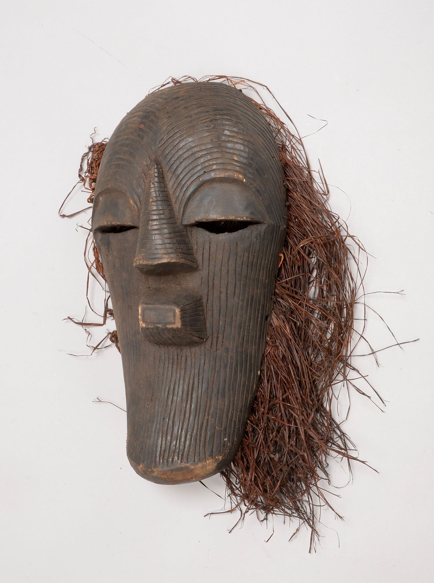 Ritualmaske, Holz geschnitzt, längl. Form, mit Rillenstruktur und Bast-Haaren