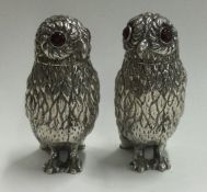 A pair of silver peppers in the form of owls with red eyes.
