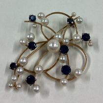 A pearl and sapphire scroll brooch in 18 carat gold mount.