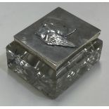 A silver and glass stamp case embossed with cherubs.