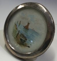 A circular silver picture frame with scene of yacht.