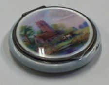 A silver and enamelled compact with village scene to front.