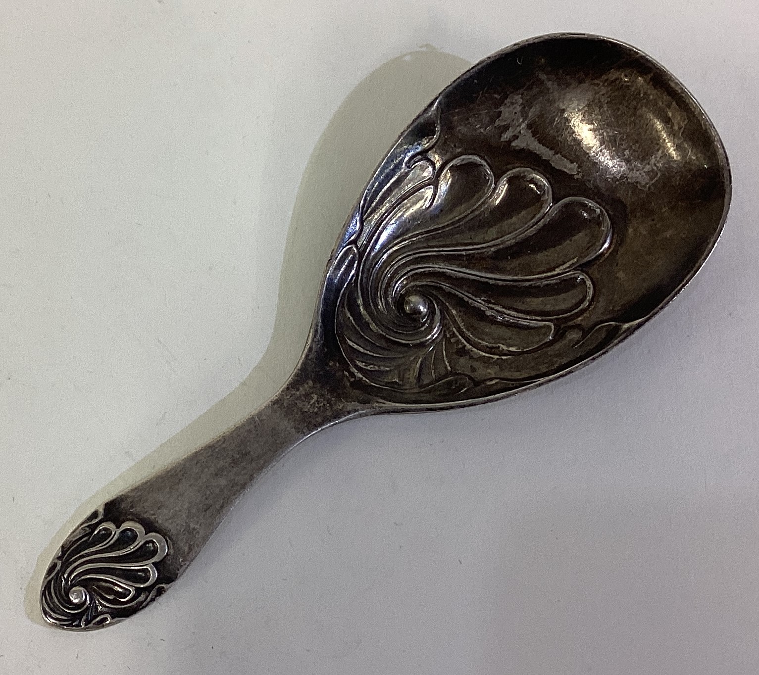 A silver caddy spoon with fluted shell design.