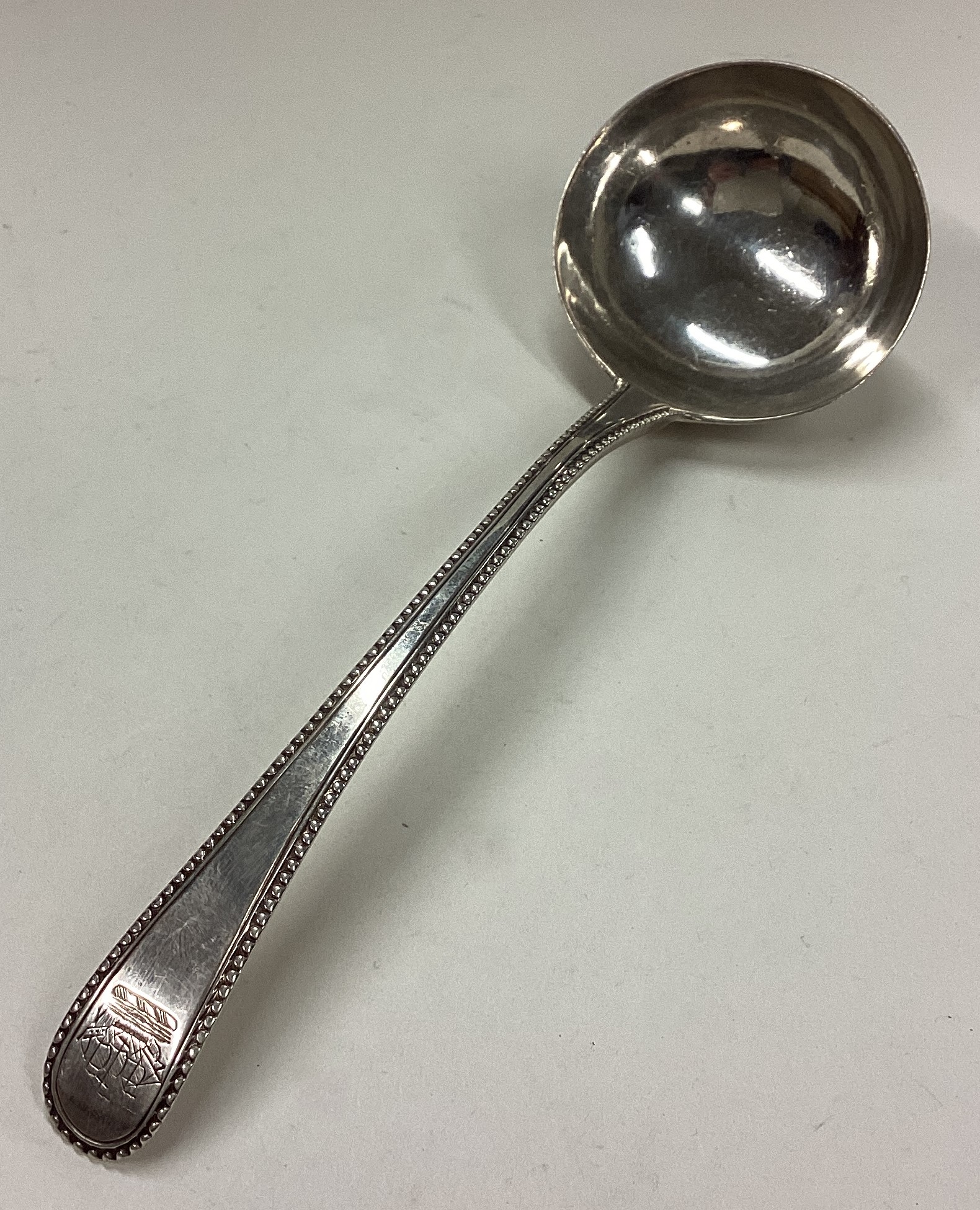 A George III silver bottom marked sauce ladle with crested and beaded decoration.