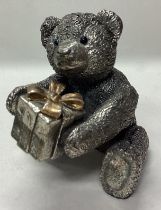 A novelty silver figure of a teddy bear holding a present.