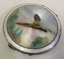 A silver and enamelled compact depicting a flying pheasant.