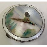 A silver and enamelled compact depicting a flying pheasant.