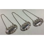 A set of three silver wine labels on suspension chains.