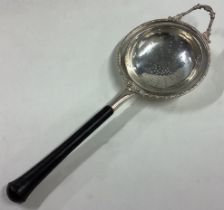 A heavy silver tea strainer with ebony handle and pierced decoration.