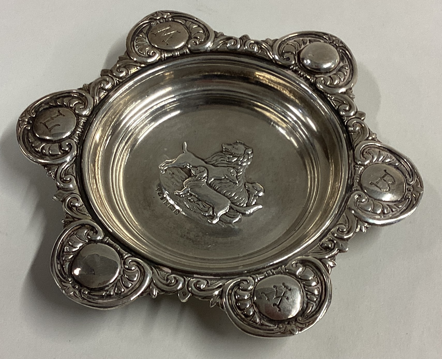 A chased silver dish with dog decoration to centre.