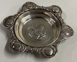 A chased silver dish with dog decoration to centre.