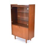 A 1970's teak cabinet, the two glazed doors with brass-finished handles, over a fall-front, on