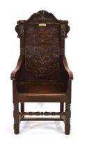 A 'Bardic' wainscott armchair in oak, the foliate carved back panel below a pair of dragons, bearing