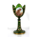 A Bohemian green glass vase of goblet form decorated with a pair of putti within a gilt fern