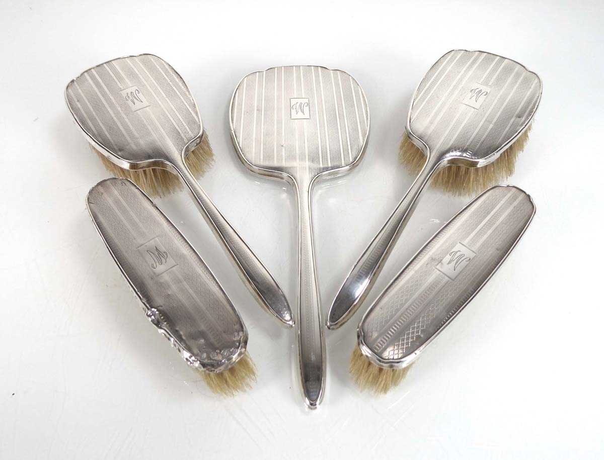 An early 20th century engine turned silver five piece dressing table set comprising a hand mirror