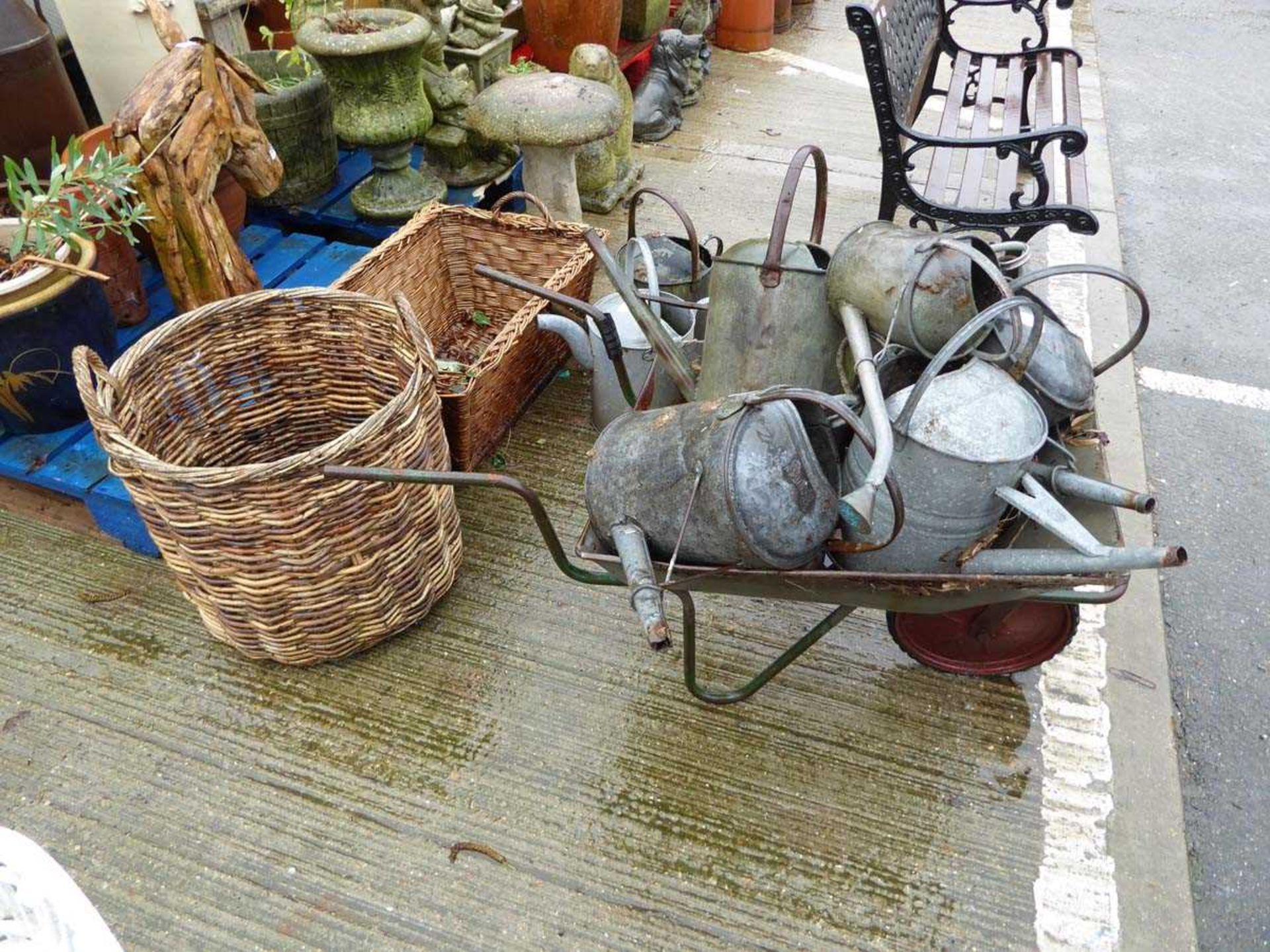 Metal wheel barrow containing galvanised watering cans and two wicker baskets