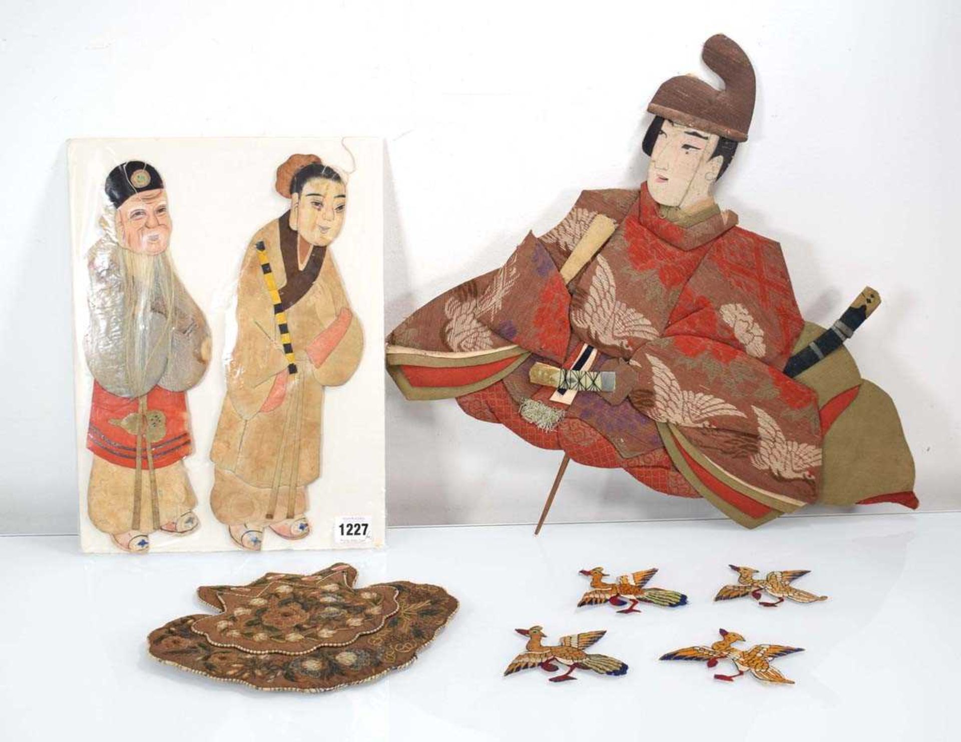 A padded fabric wall hanging modelled as a seated warrior, w. 50 cm, a further pair of figures and