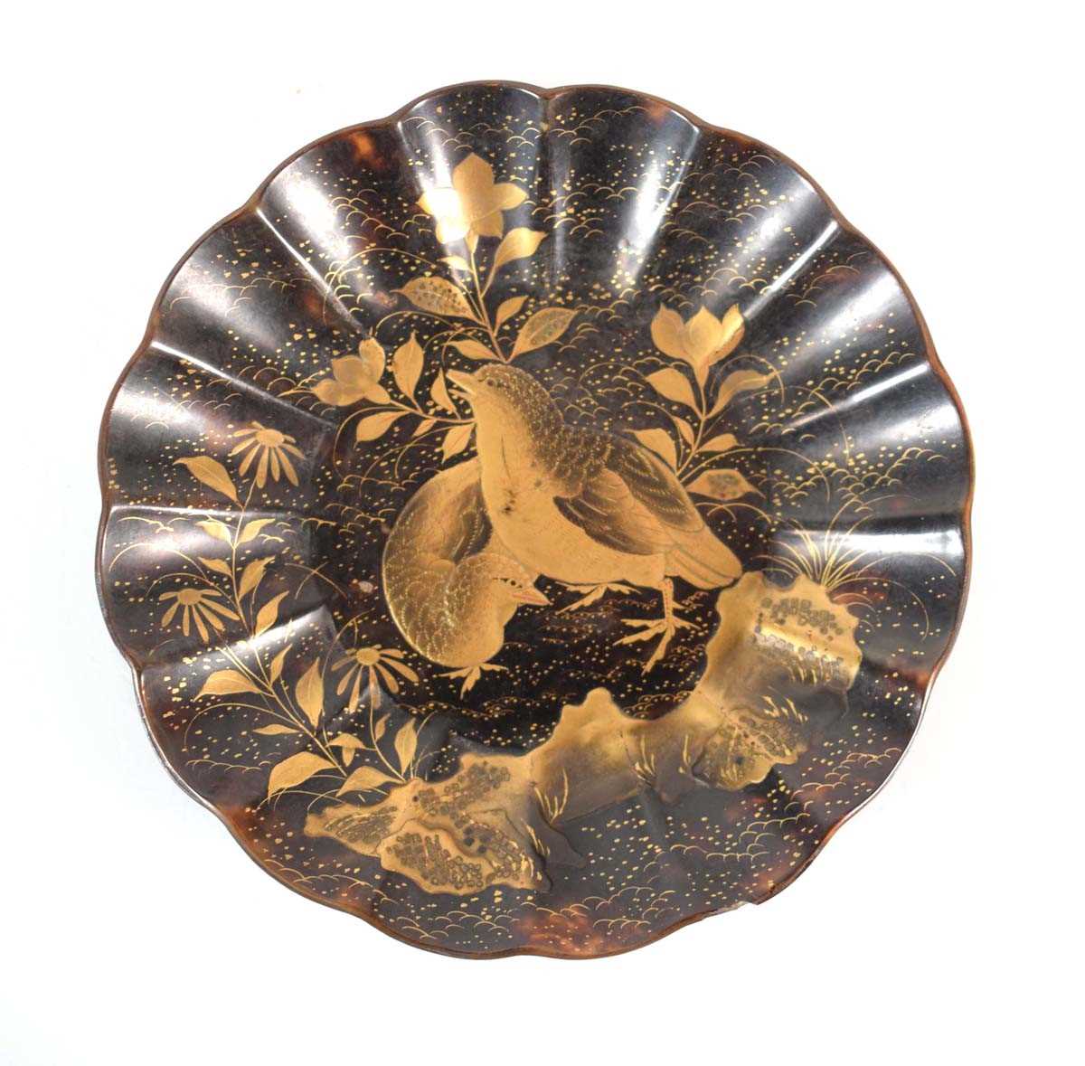 A Japanese tortoiseshell and gilt lacquered dish of flowerhead form, centrally decorated with a pair