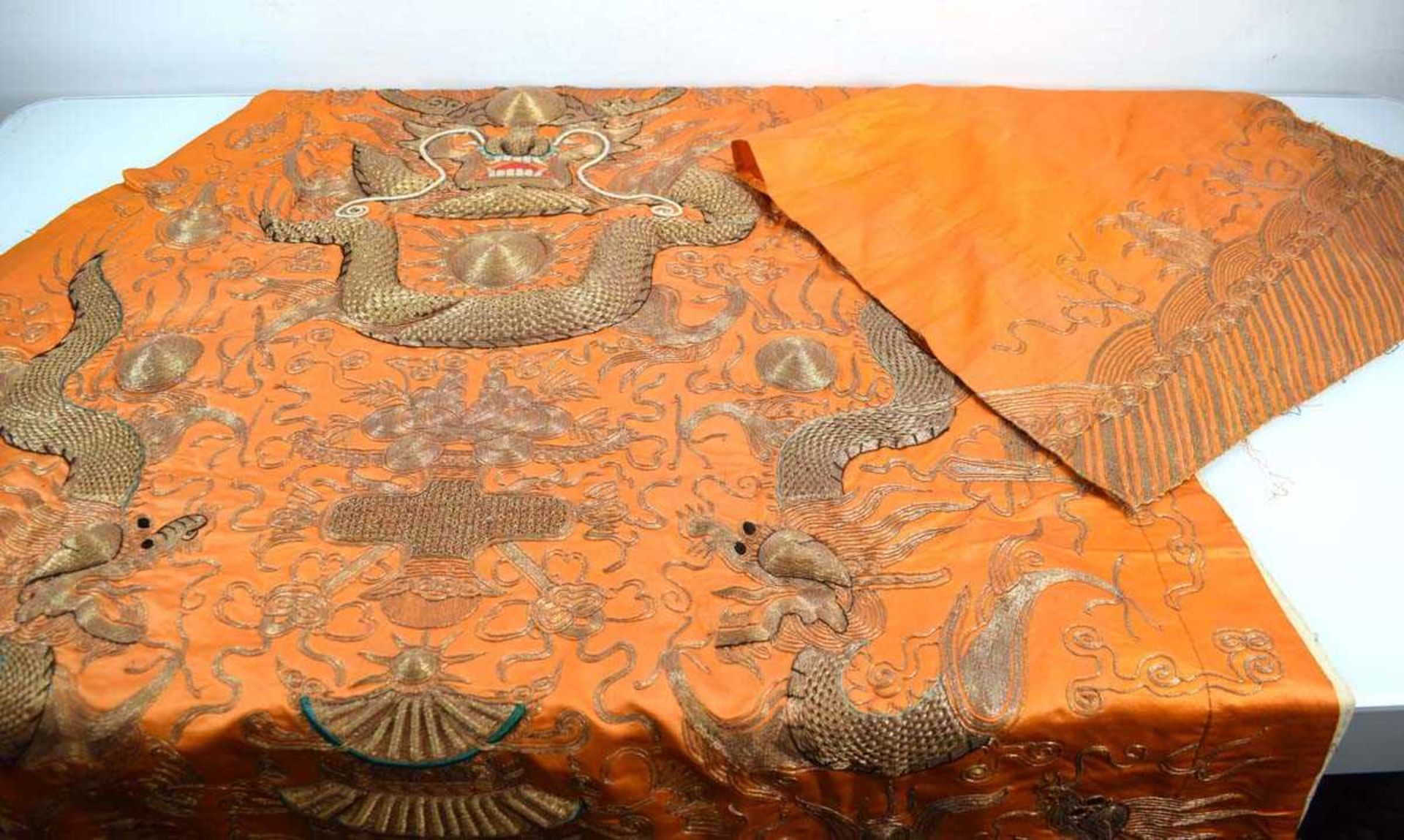 A Chinese robe section worked in gold coloured threads depicting dragons and a pagoda on an orange