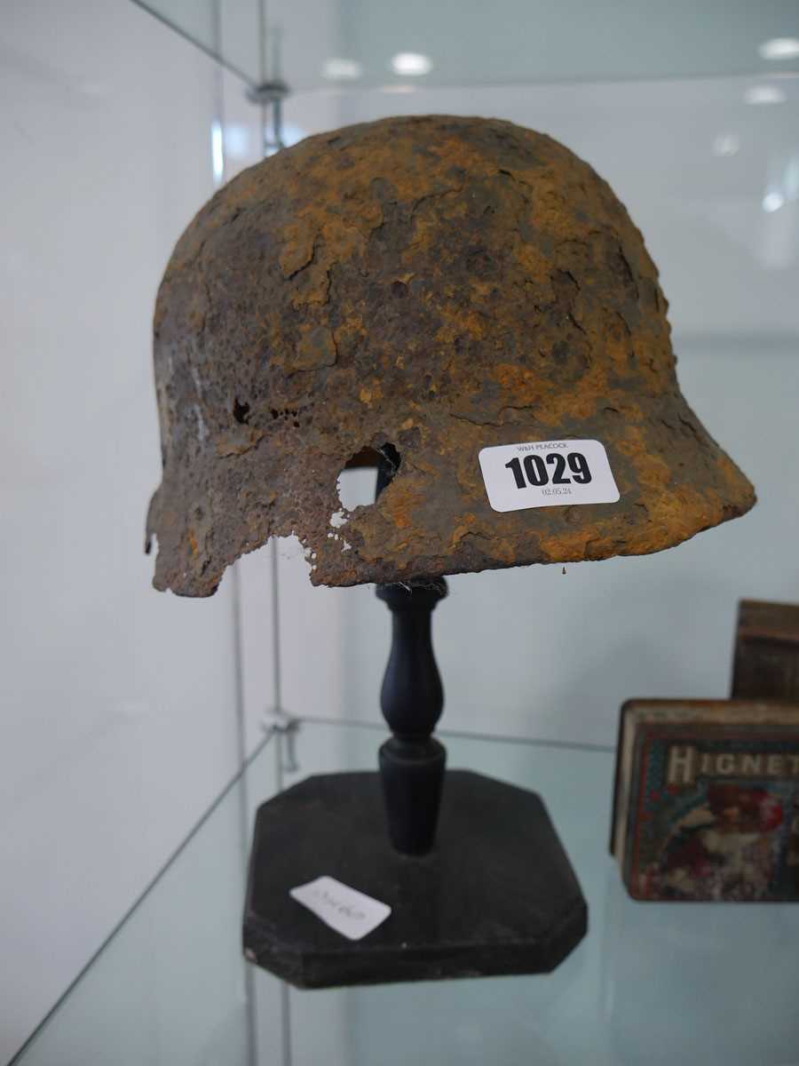 Military helmet bearing Nazi insignia on purpose built wooden stand Heavy rusting and deterioration